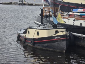 Klassieke sleepbootje met zwarte romp en crèmekleurige kajuit.
