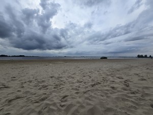 Zandstrand aan een groot meer met steigers.